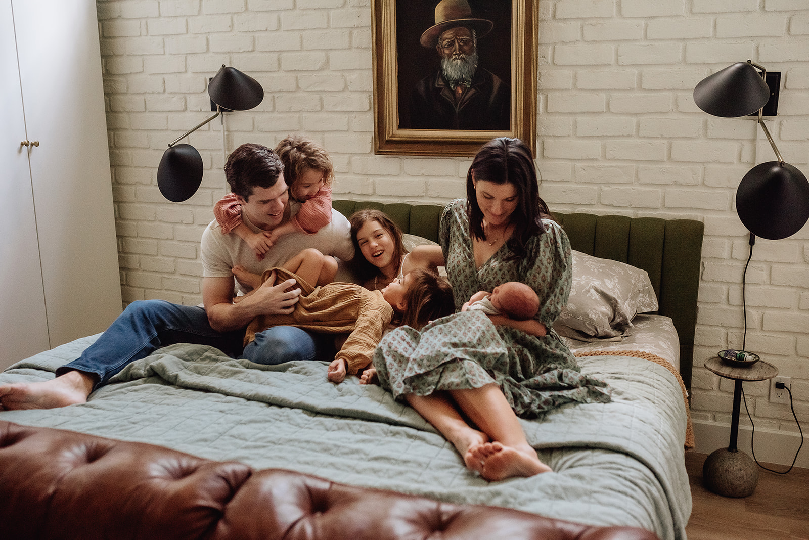 A mother sits on a bed holding her newborn baby while her partner plays with their three other daughters next to her Baby and Kids 1st