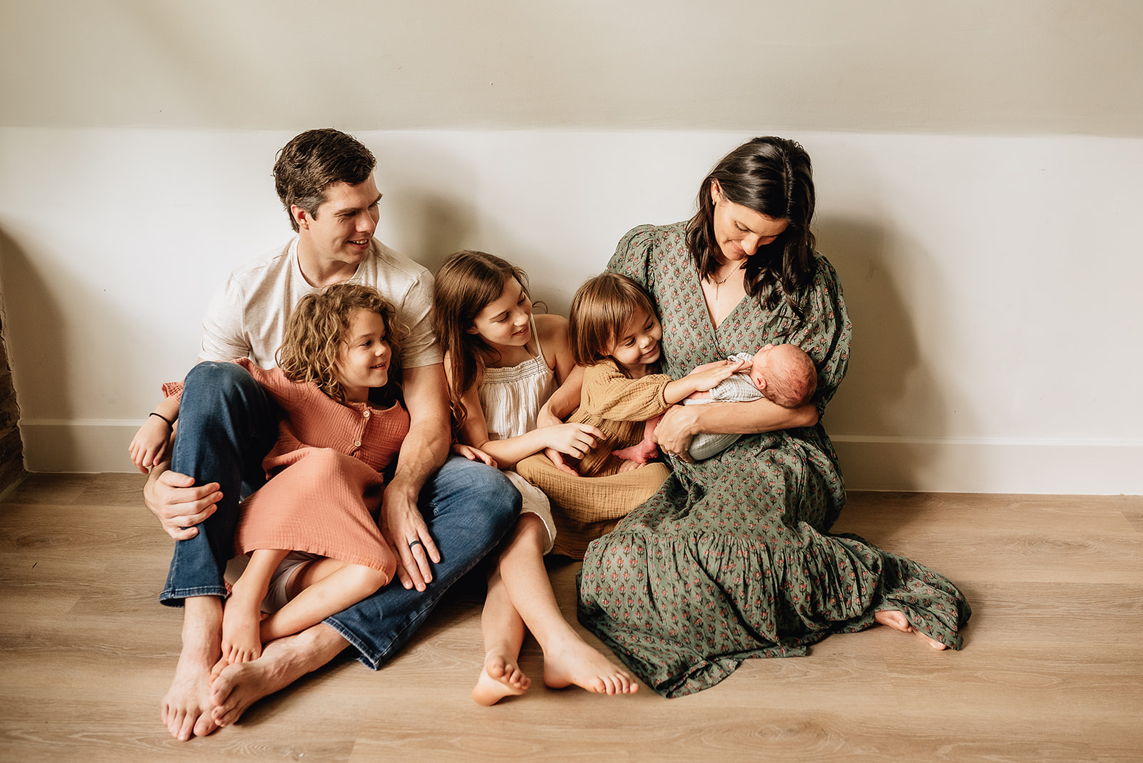 A family of six sits on the floor looking down on and touching their newest member in mom's arms
