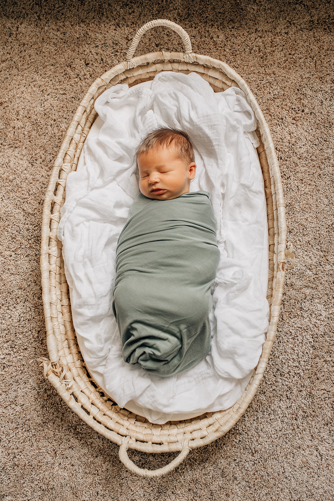 A newborn baby sleeps in a green swaddle while laying in a woven basket on the floor Cy Fair Birth Center