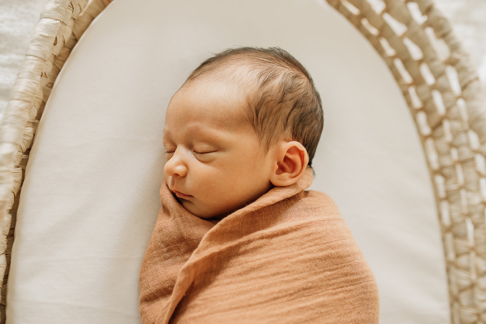 A newborn baby sleeps in a woven basket in an orange swaddle Houston baby shower venues