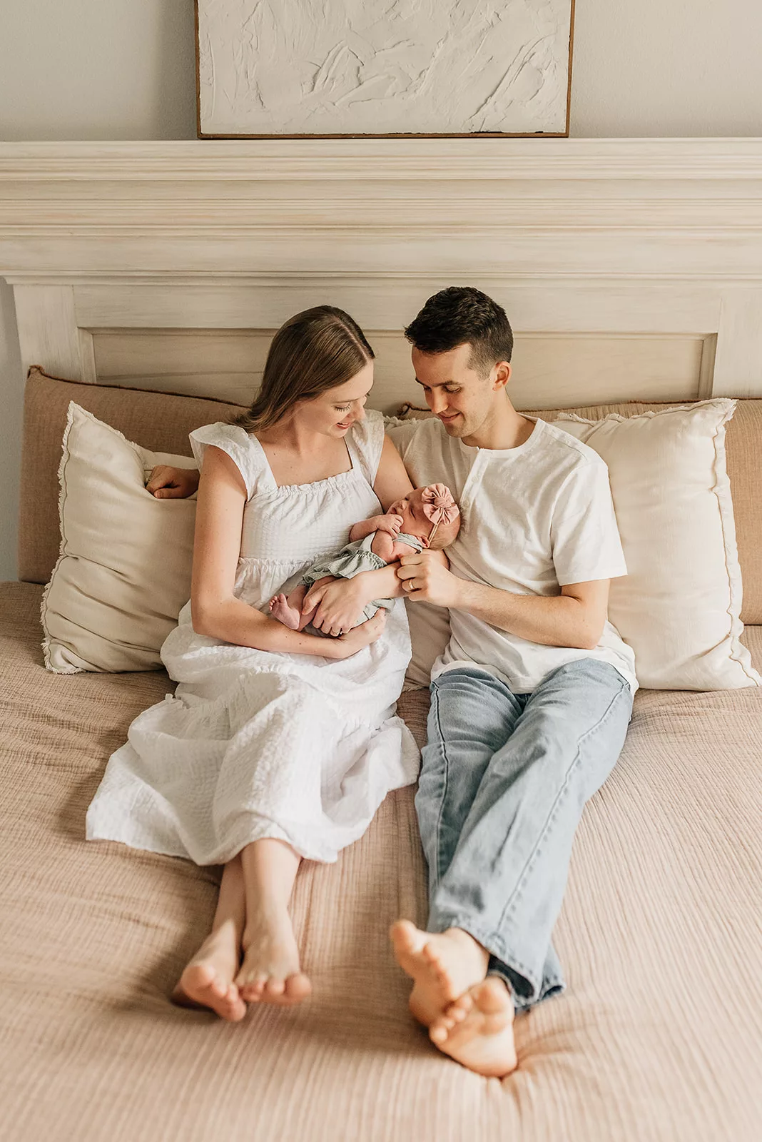 New parents sit together on a bed while they gaze at their newborn baby daughter