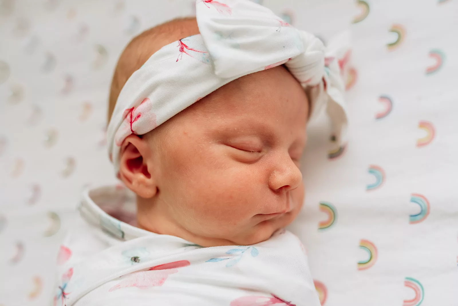 Details of a sleeping newborn baby in a colorful swaddle and bow