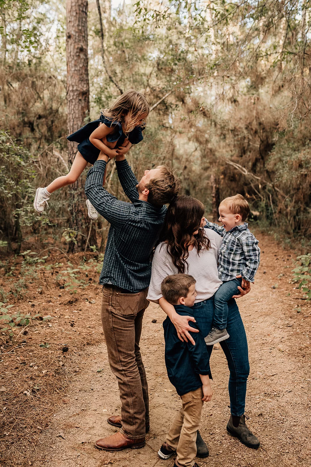 Mom and dad lift and play with their three young children in a forest trail Houston Baby Boutiques