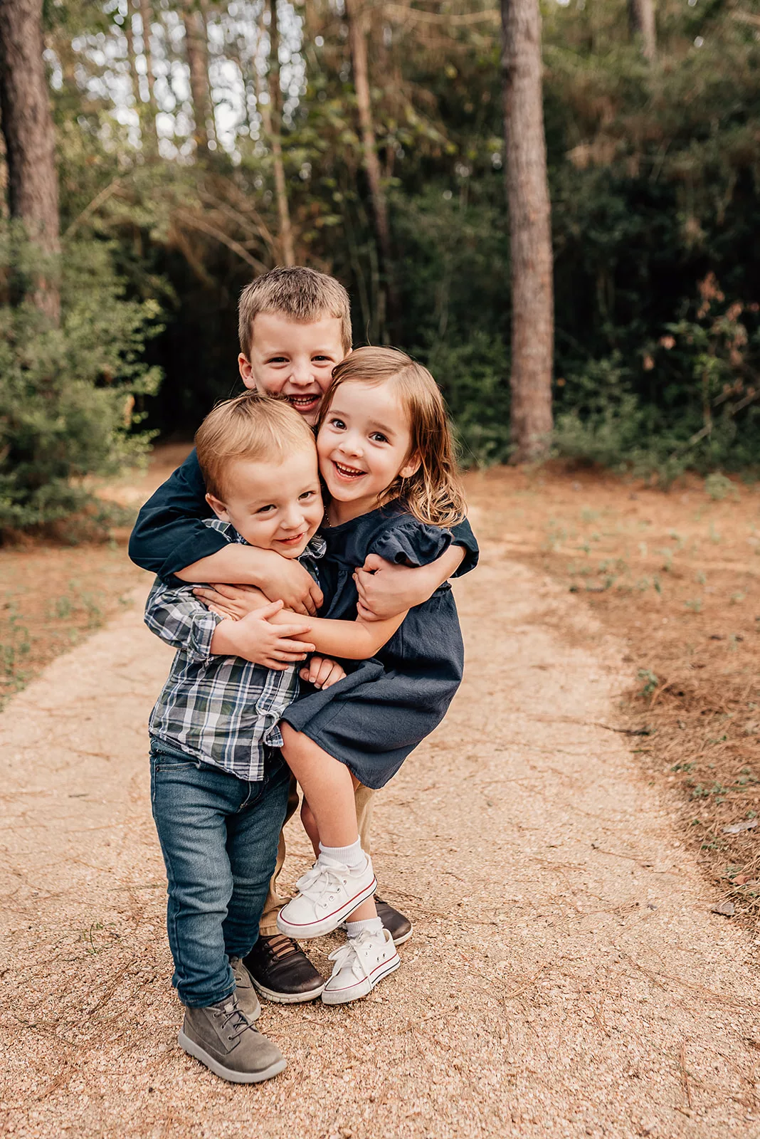 Three sibling hug and smile while standing in a forest trail