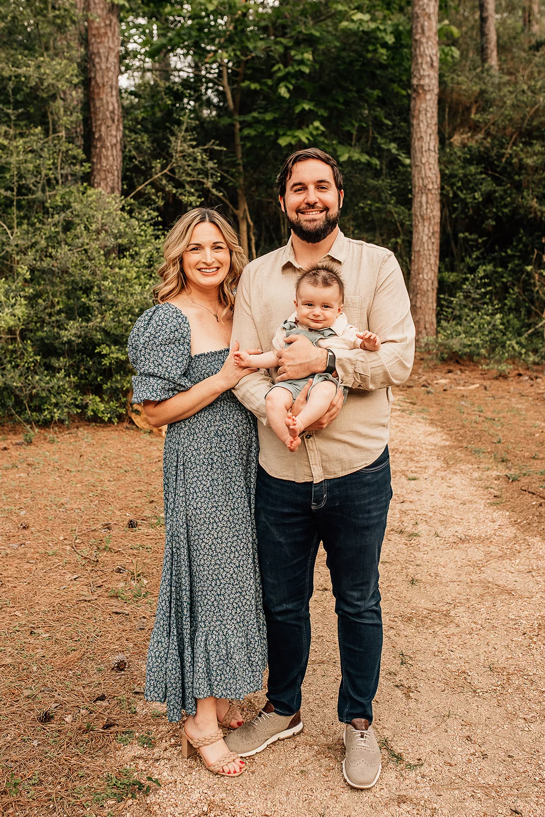 A father stands in a forest trail holding his happy infant son with his wife holding onto his arm next to him
