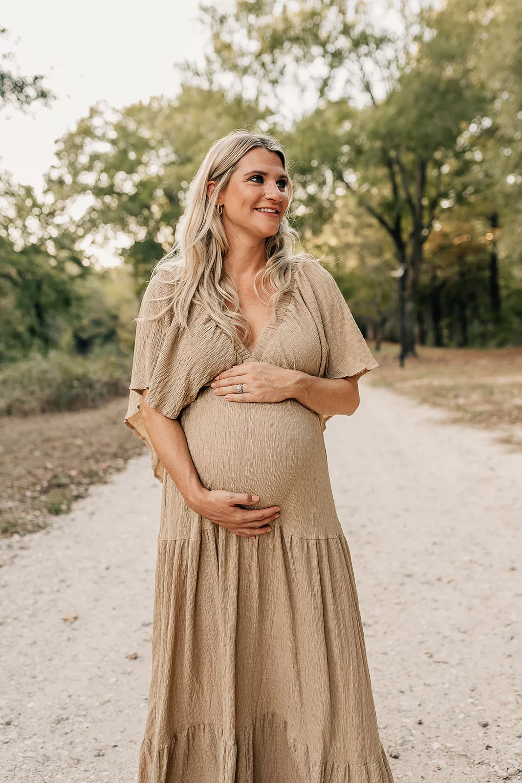 A mom to be smiles while walking down a park path holding her bump before meeting a Houston Postpartum Doula