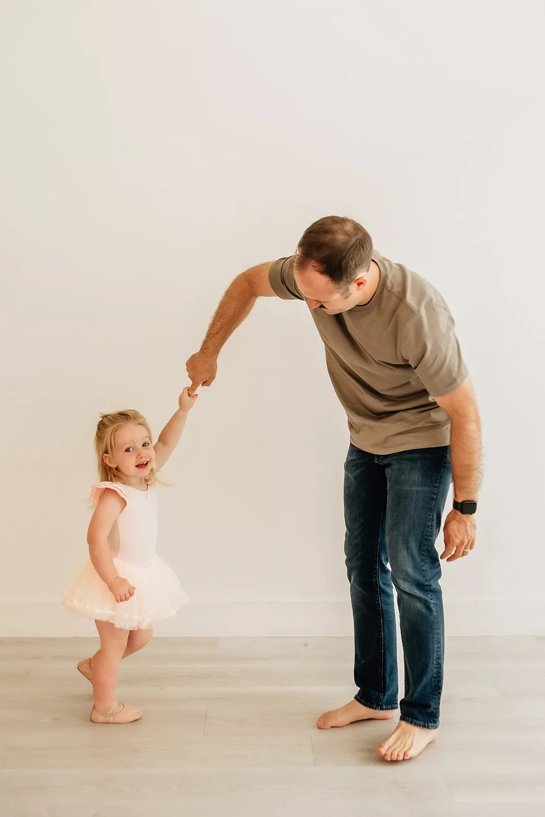 A father dances and twirls his toddler daughter in a pink tutu in a studio after visiting Houston Daycares