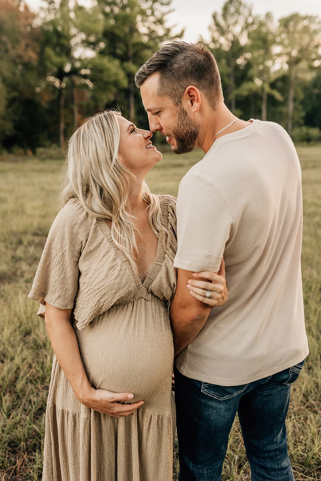 Expecting parents lean in for a kiss and hold the bump while standing in a field at sunset thanks to Houston Fertility Clinics