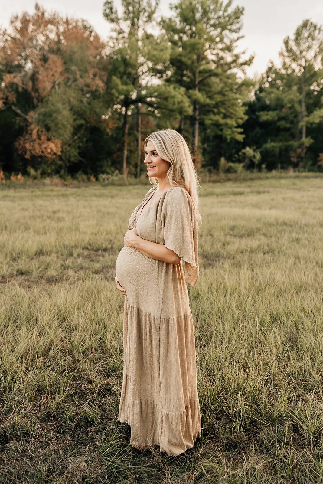 A mom to be stands in a field at sunset in a brown dress holding her bump after using Houston Fertility Clinics