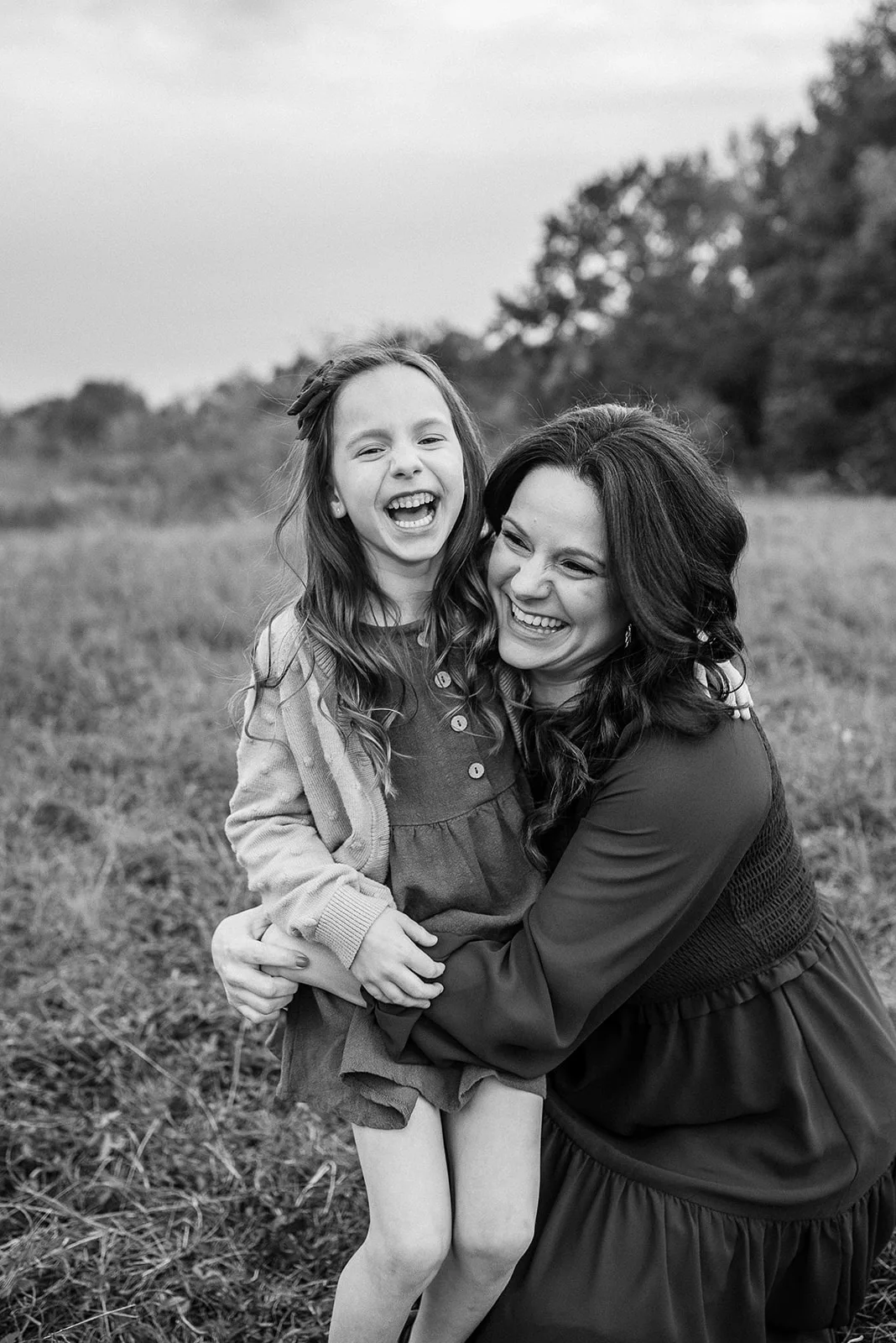 A mother and daughter laugh while hugging in a park field in black and white after visiting Houston Pediatric Dentistry