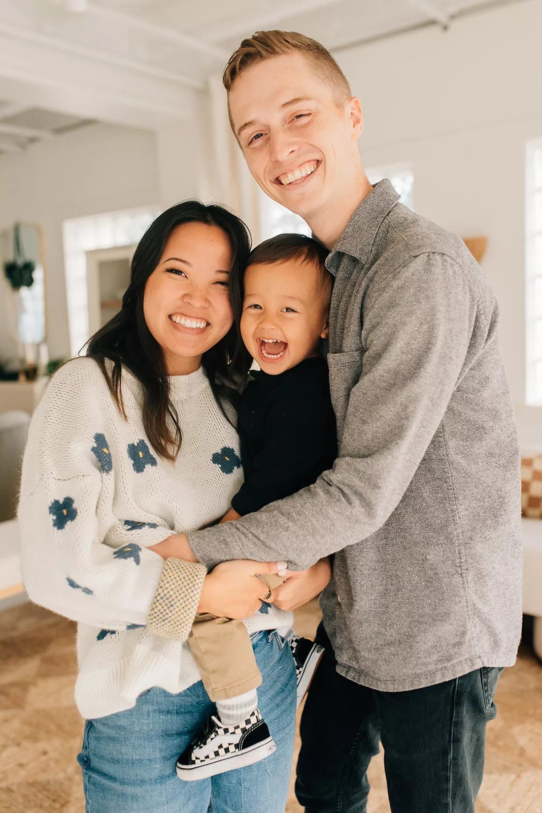 Happy parents stand in a living room holding their toddler son while laughing together after meeting Houston Babysitters