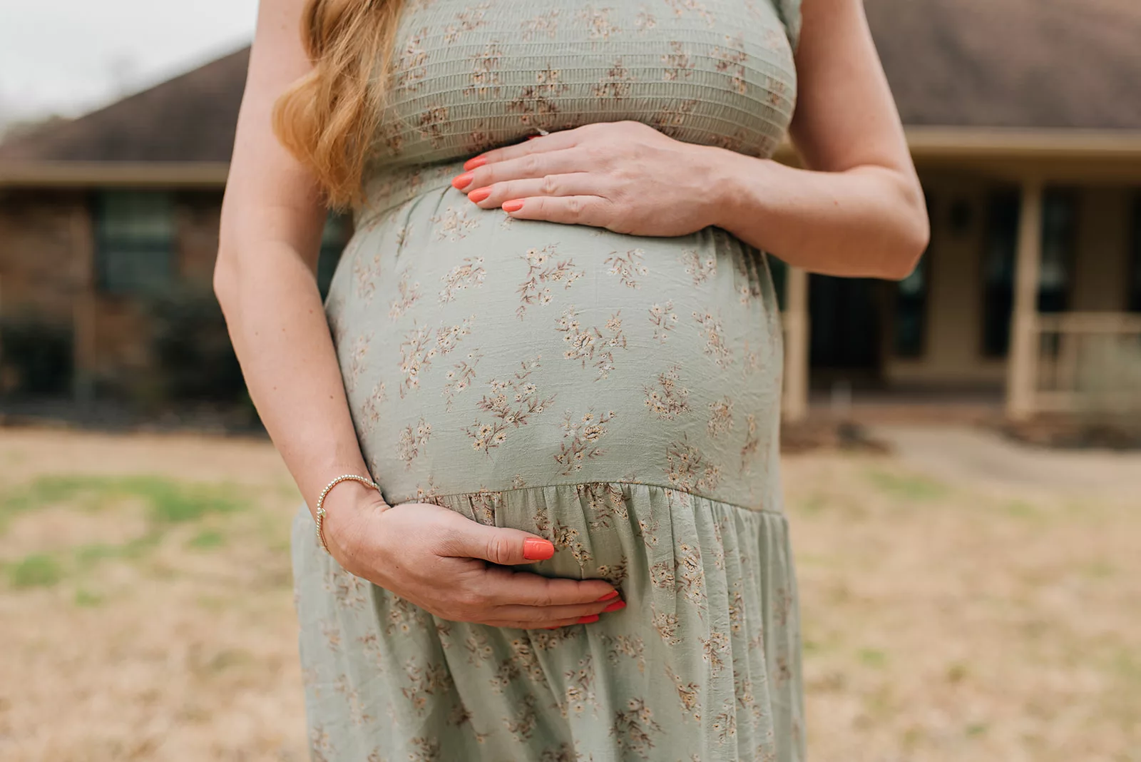 Details of a mother to be in a green floral print dress holding her bump after finding a Houston OBGYNs